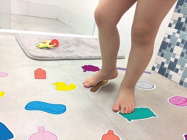 Adesivo para piso antiderrapante com desenhos coloridos de objetos de banho aplicados em piso claro de banheiro, mostrando detalhes para aplicação.